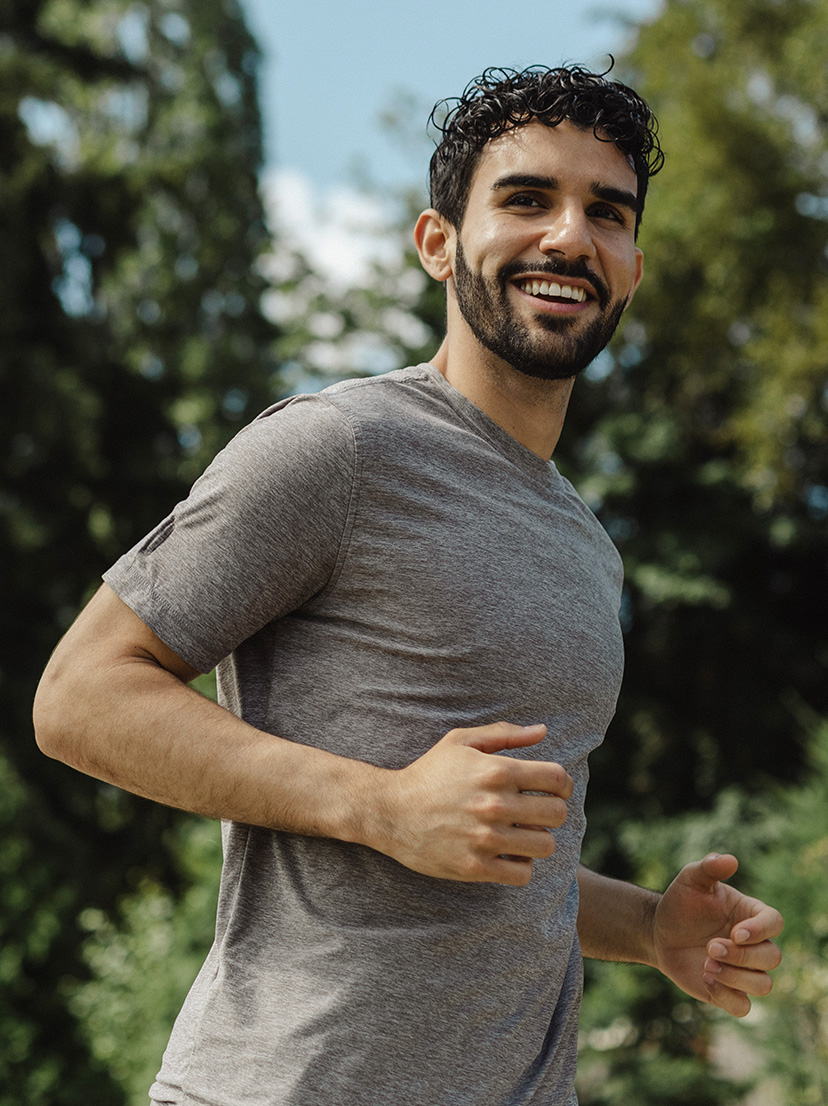 A young man with dark curly hair jogging outdoors, smiling