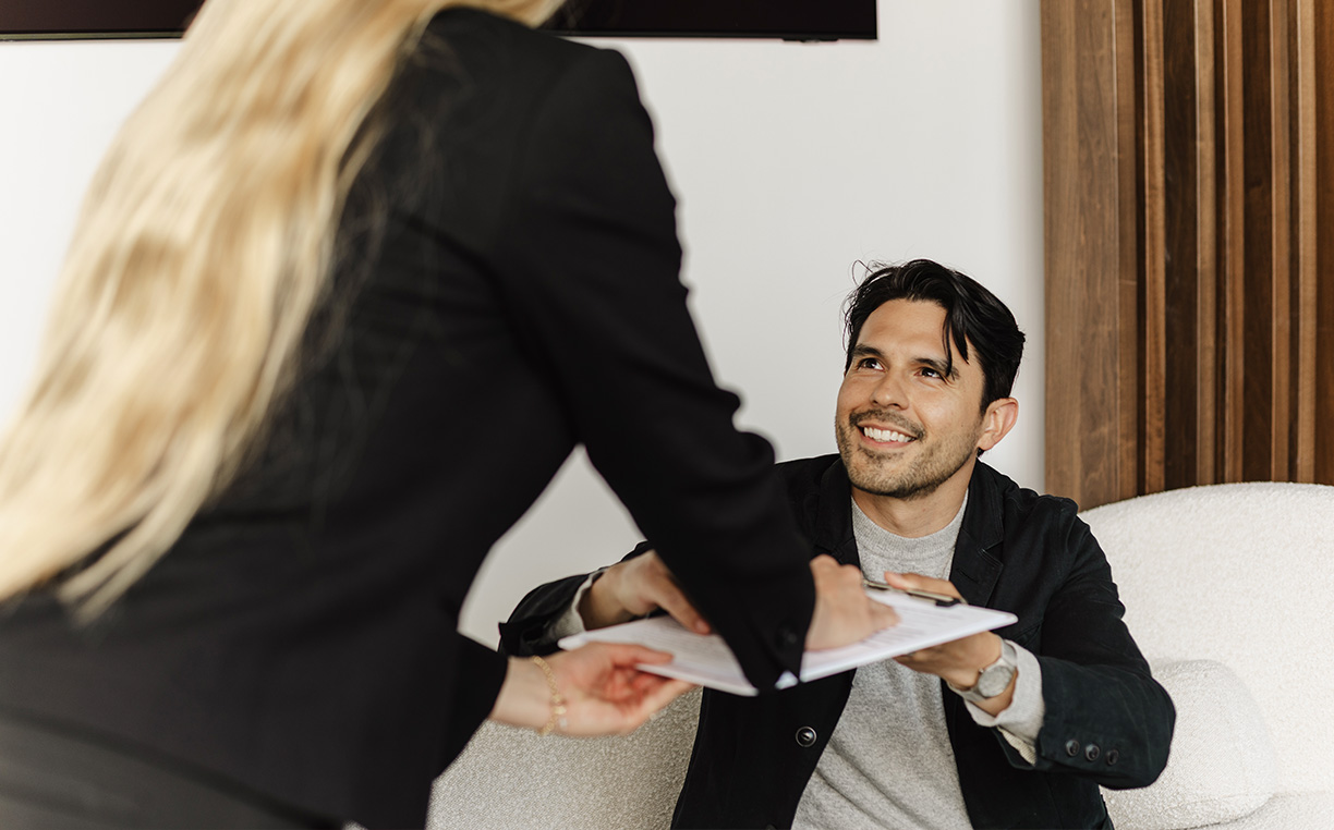 A staff member handing paperwork to a smiling seated patient