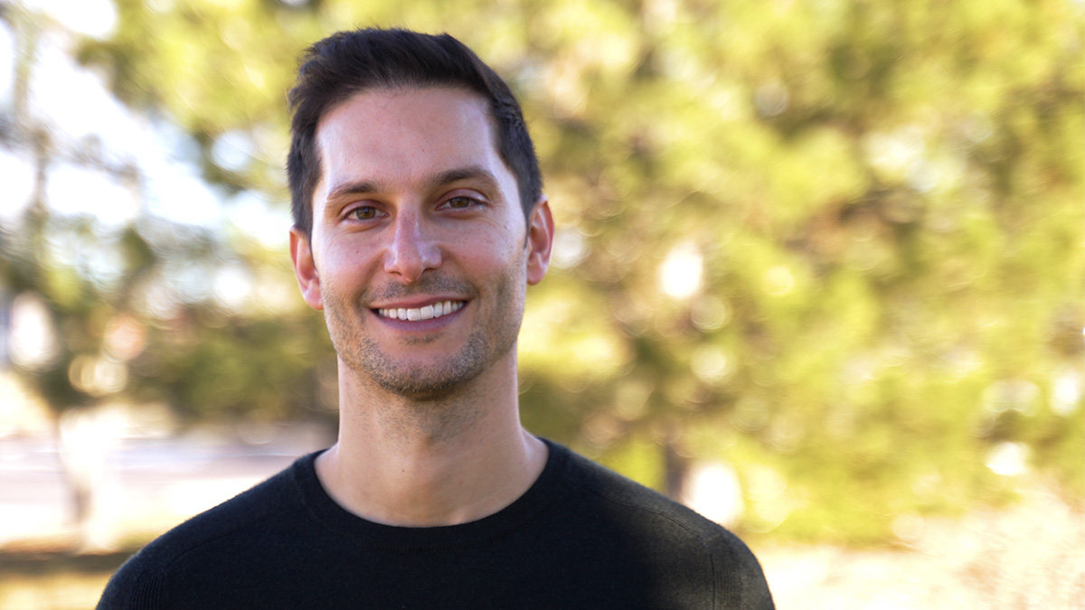Nick Harper smiling at the camera outdoors, trees blurred behind him