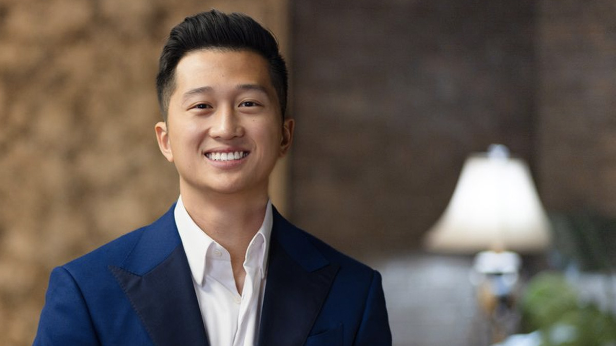 Timmy Chiu smiling in a navy blazer and open white shirt, warm interior behind him